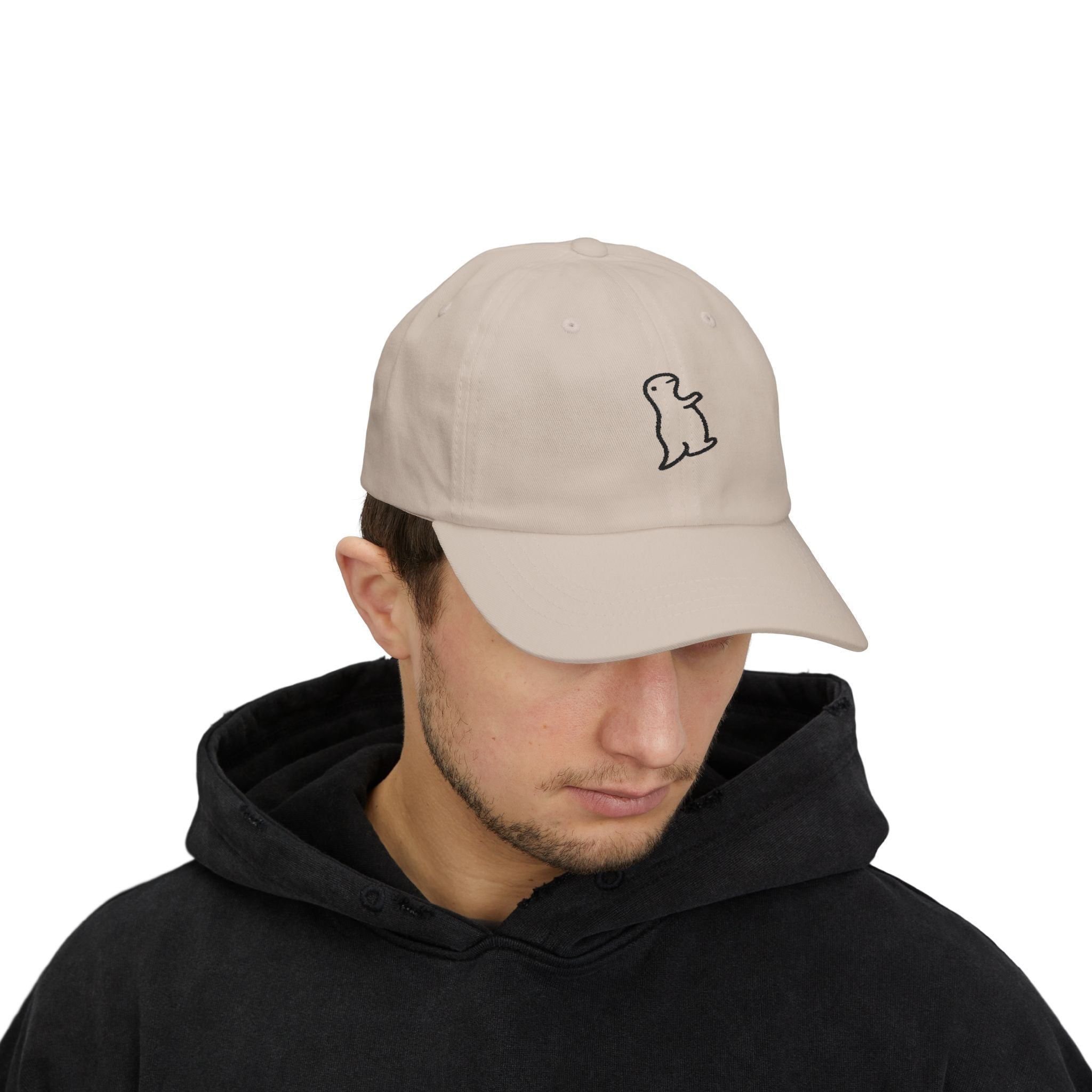 TUCURUCU beige 6-panel cotton cap with a small embroidered character on the front, worn by a man in a black hoodie.